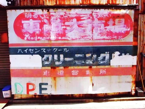 Rust and peeling paint obscure red, white and blue advertising on a large roadside sign.