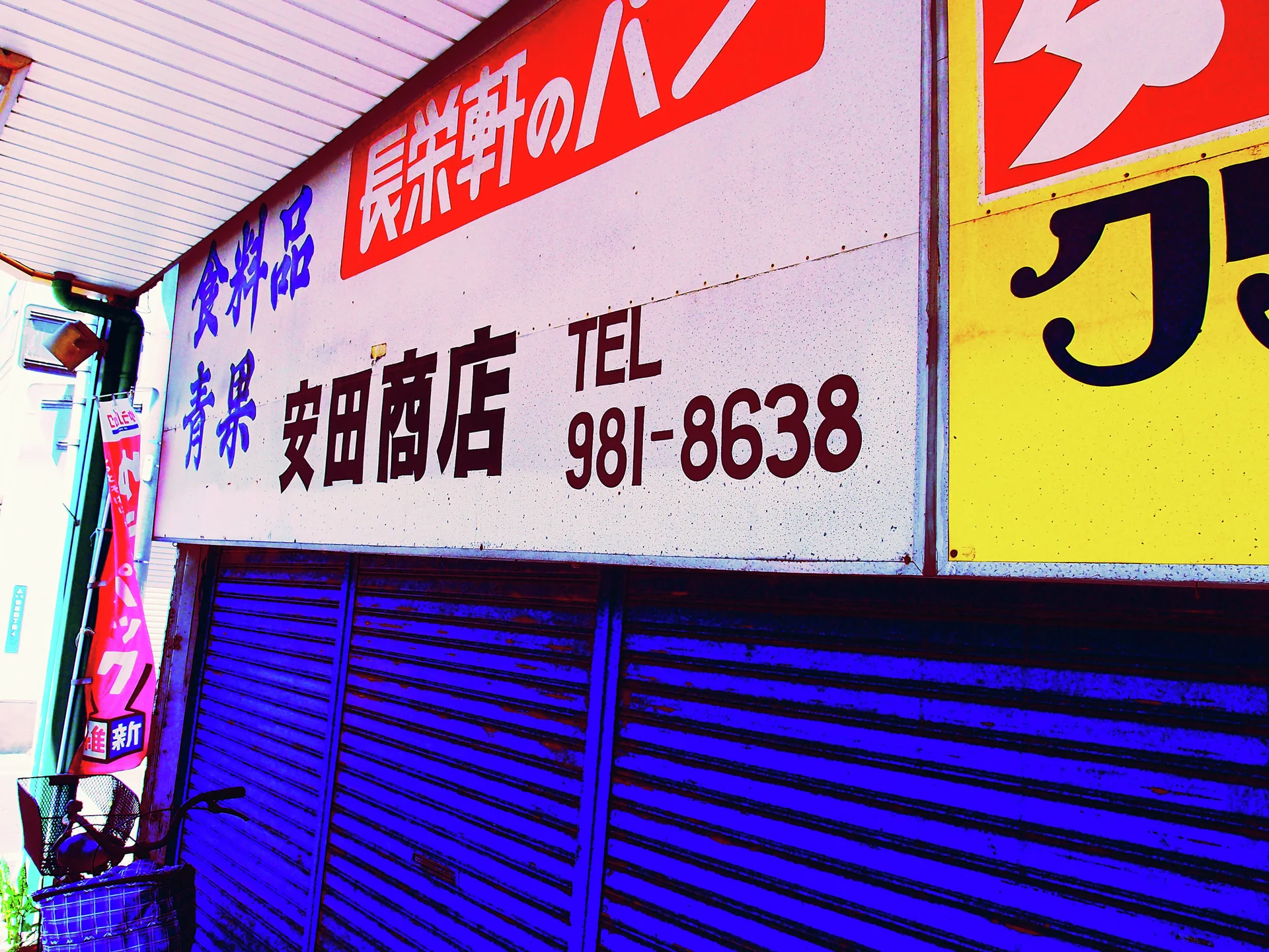 A long pale shop sign with Japanese lettering and a phone number hangs above vivid blue shutters.