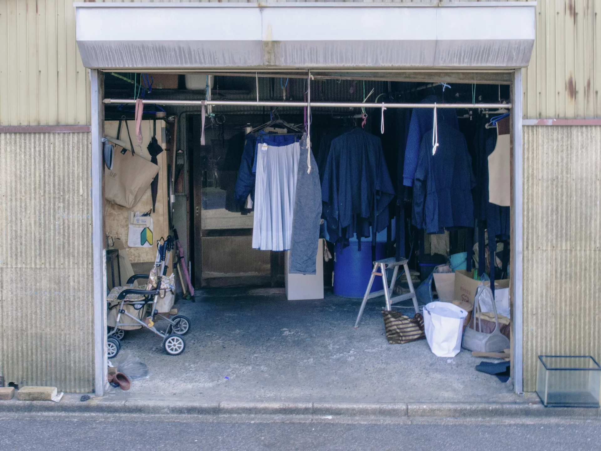 Dark blue and white garments hang across an open garage containing a stroller, stepladder, and containers.