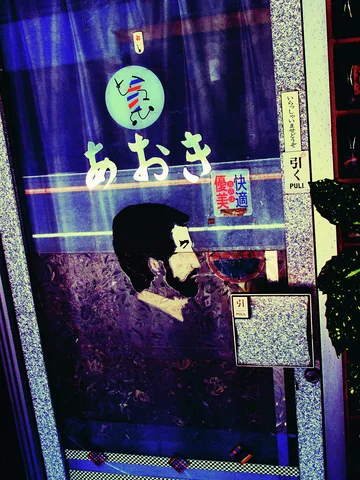 A dark glass door bears pale Japanese lettering and a painted man's profile beneath a small circular emblem.