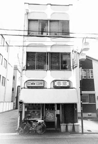 Rounded facade details frame dark upper windows above a shop entrance and bicycles in black and white.