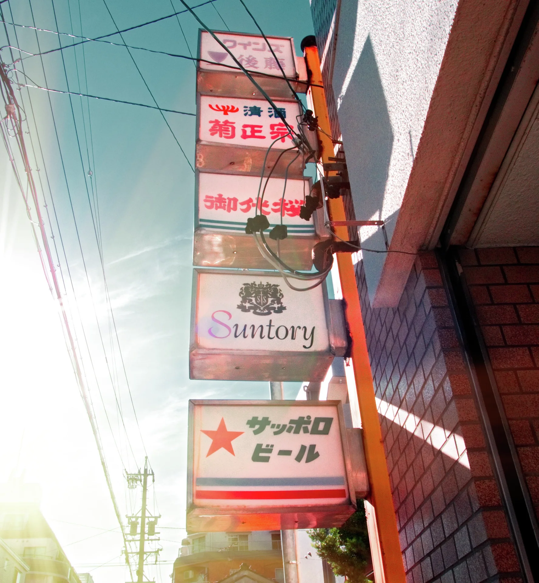 Stacked rectangular restaurant and drink signs project beside a tiled wall under overhead wires.