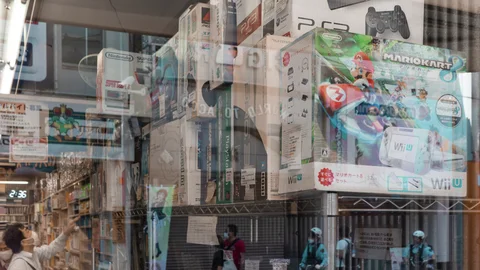 Street reflections overlap colorful character advertisements on a glass storefront above passing pedestrians.