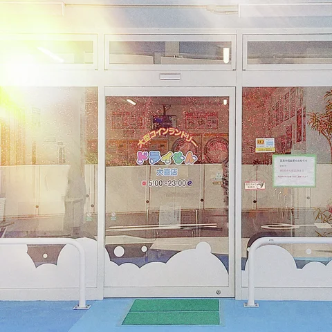 Sunlight flares across glass shop doors with a small Open sign and scalloped white lower panels.