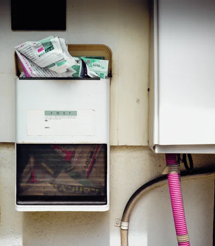 Paper packets protrude from a white wall-mounted box beside exposed pipes and a pink flexible hose.