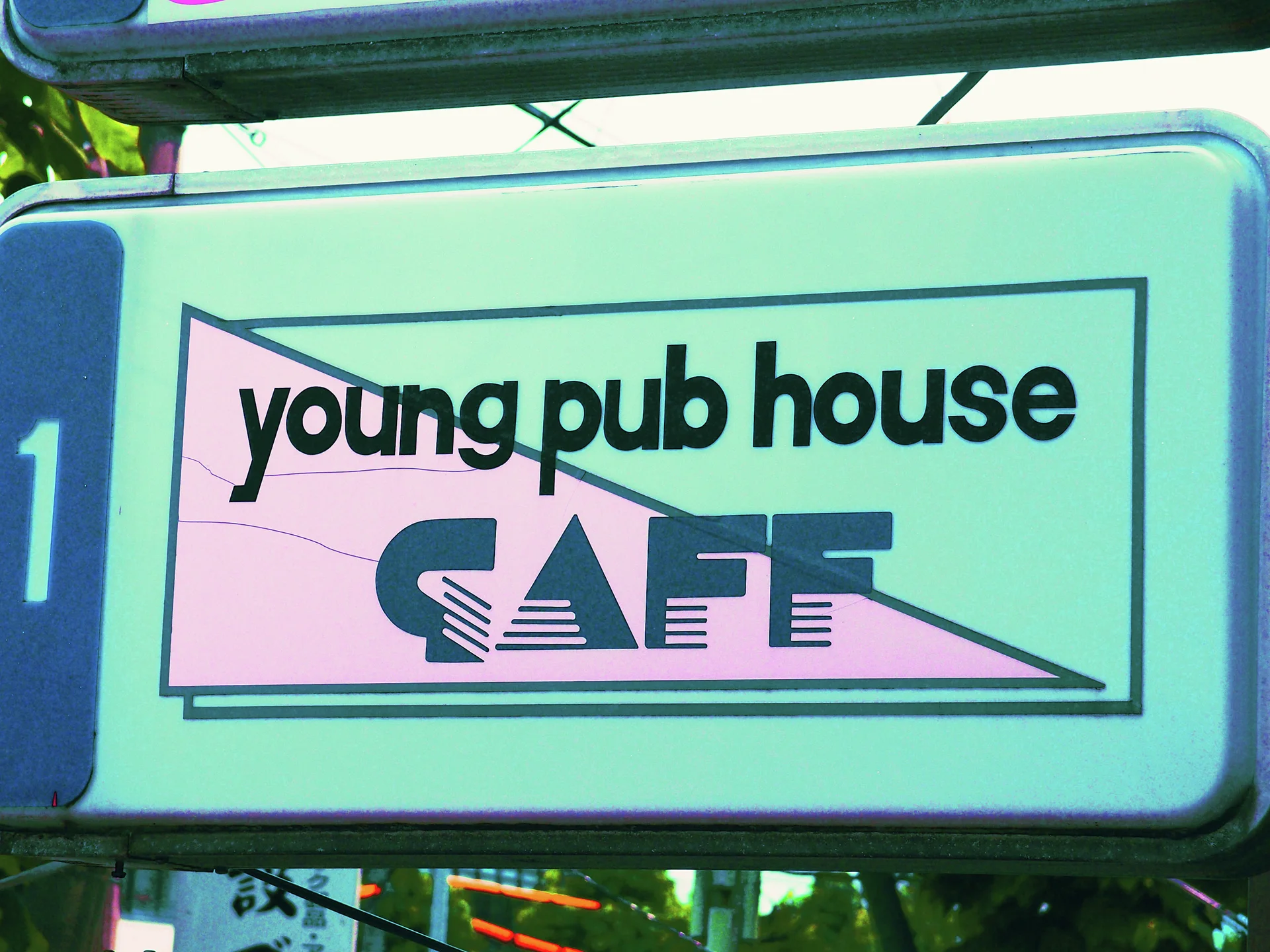 A rectangular pub sign features bold black lettering over a pink triangular background.