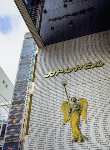 A gold winged figure decorates a tall white brick-patterned facade beneath raised Japanese lettering.