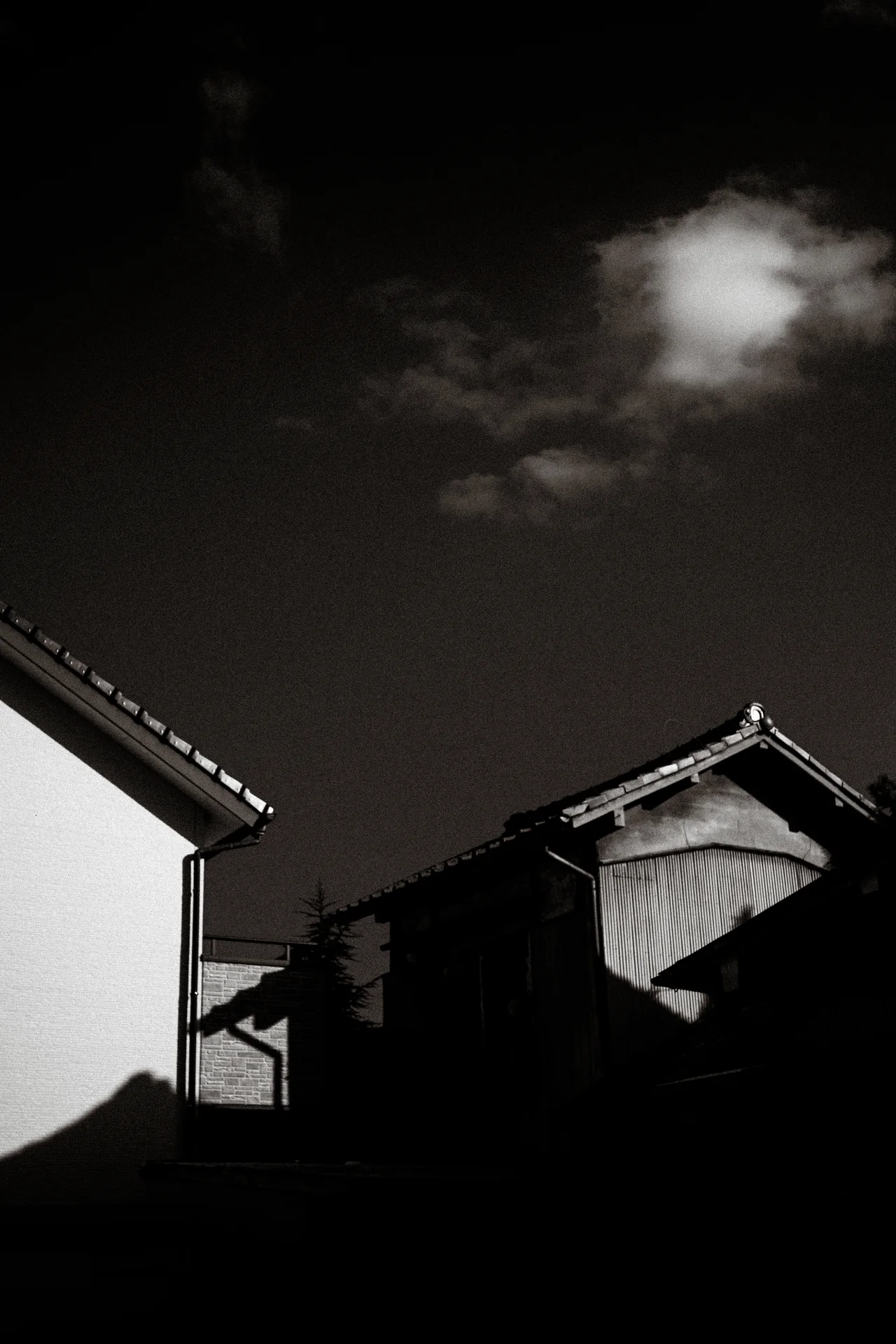 Small houses form dark angular silhouettes beneath a bright isolated cloud in monochrome.