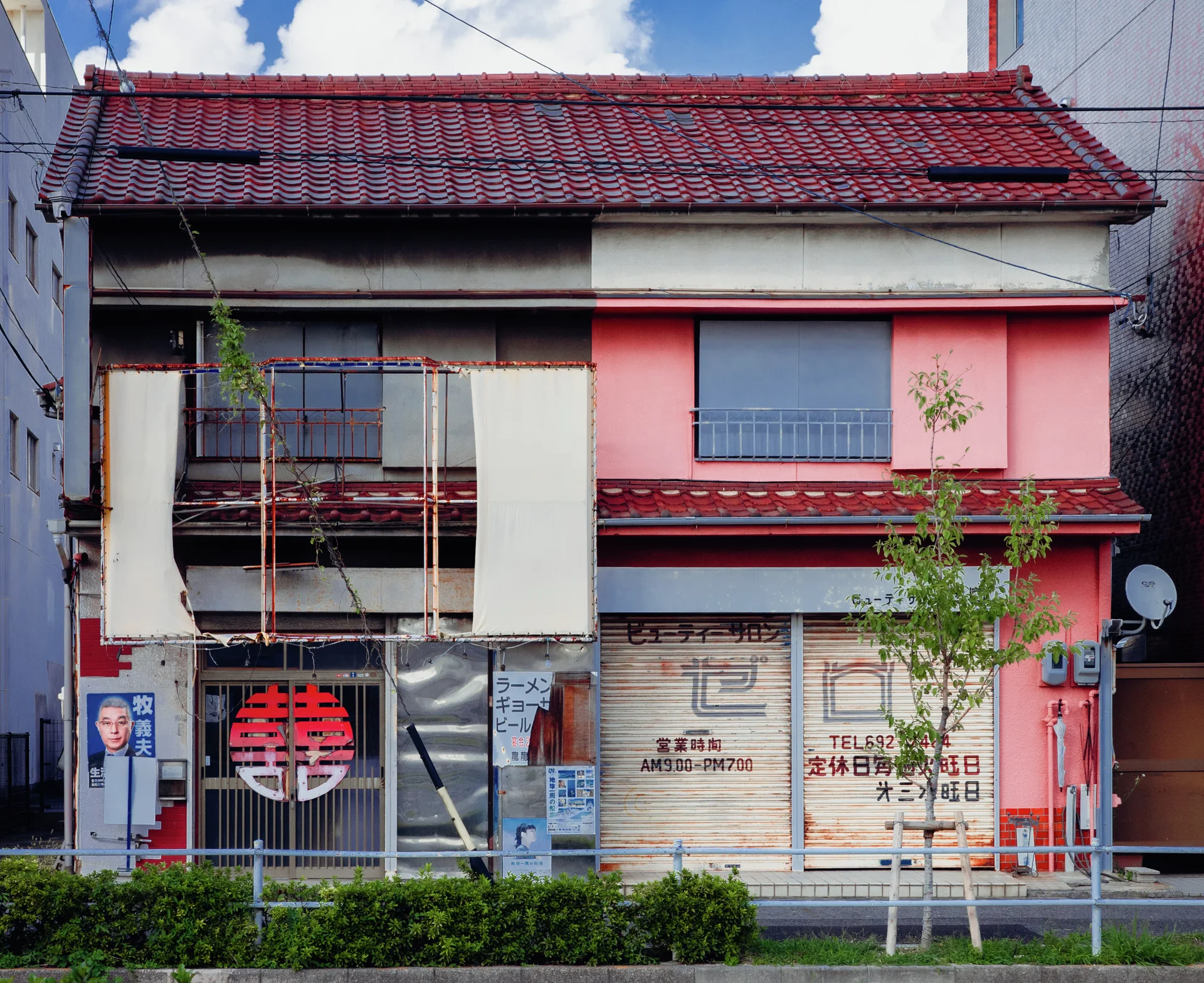 A weathered two-story building combines pink walls, closed shop shutters, and a red tiled roof.