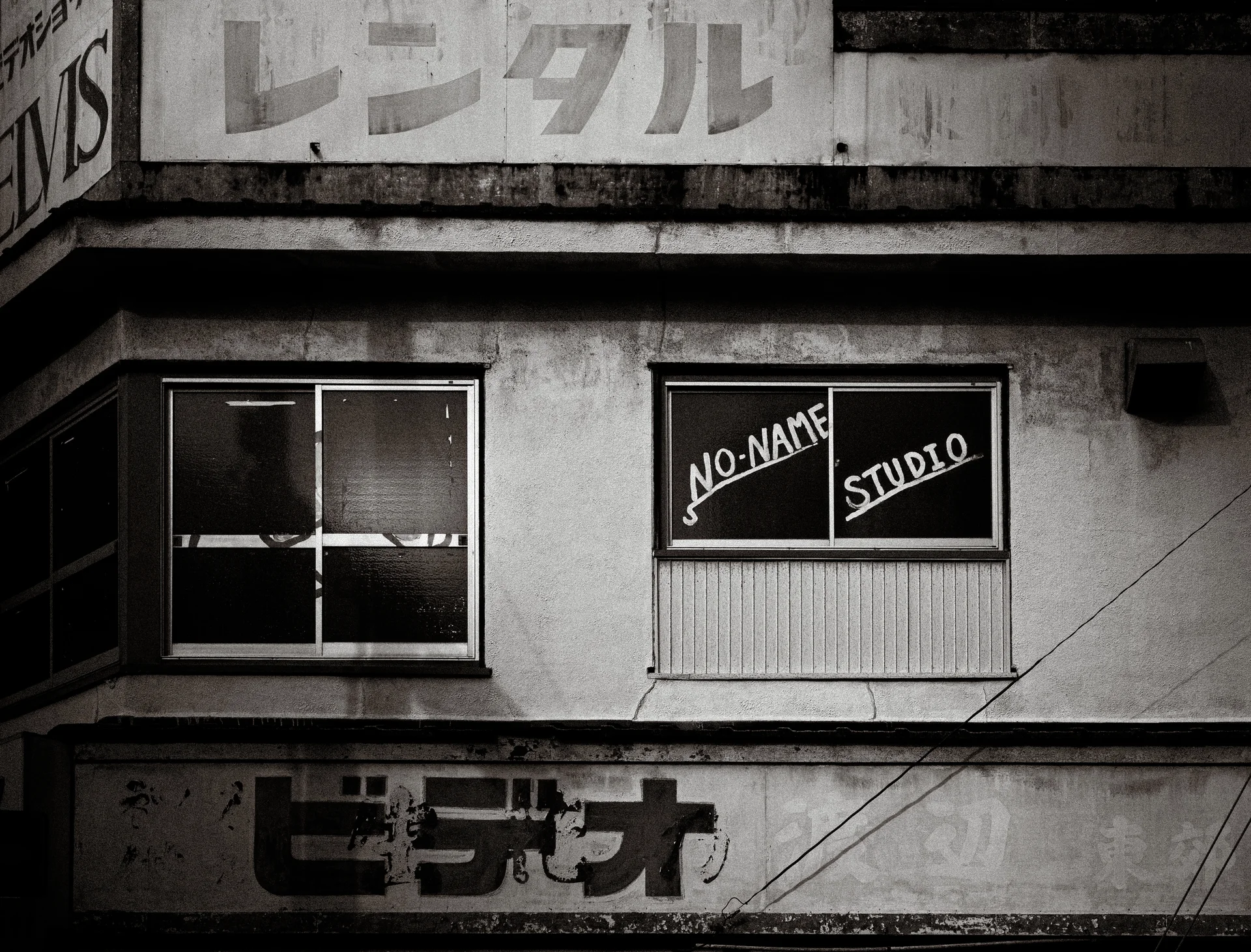 Studio lettering decorates an upper window above weathered storefront signs in black and white.
