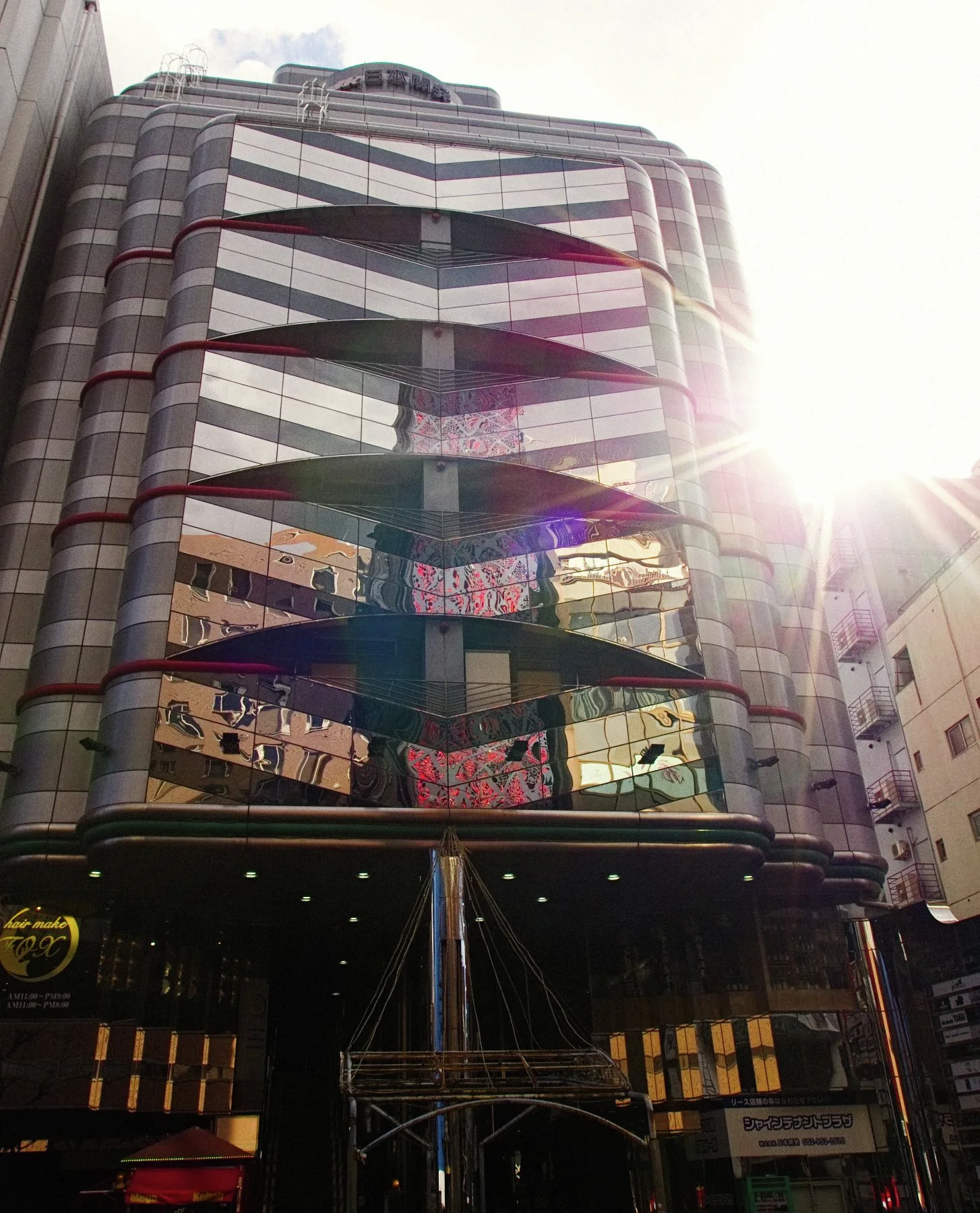 Repeated triangular window bands climb a tall building with sunlight flaring along its right edge.