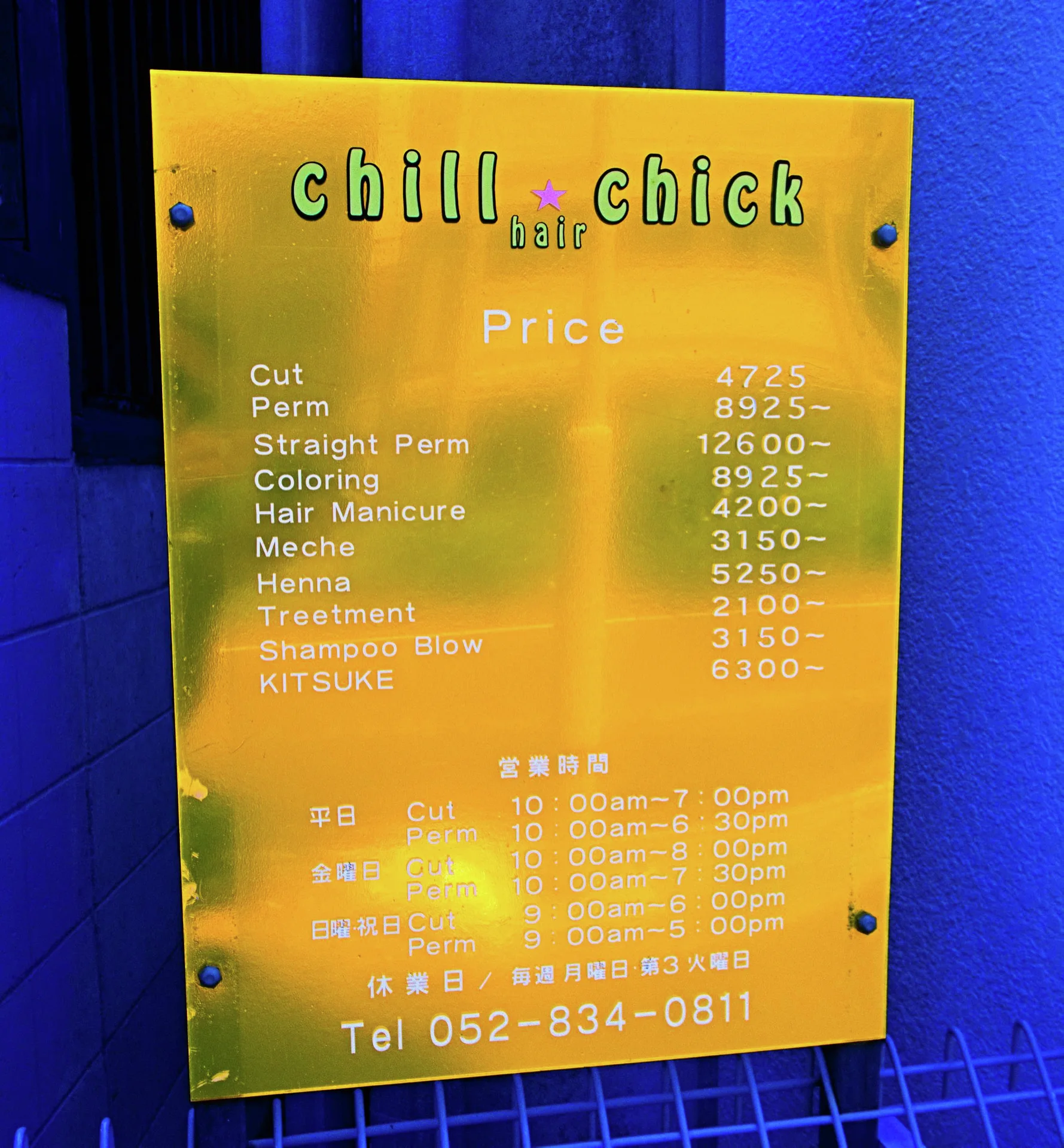 A reflective gold salon price plaque is mounted against a vivid blue wall.