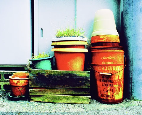 Terracotta pots and a red printed bucket rest beside a weathered wooden planter against a wall.