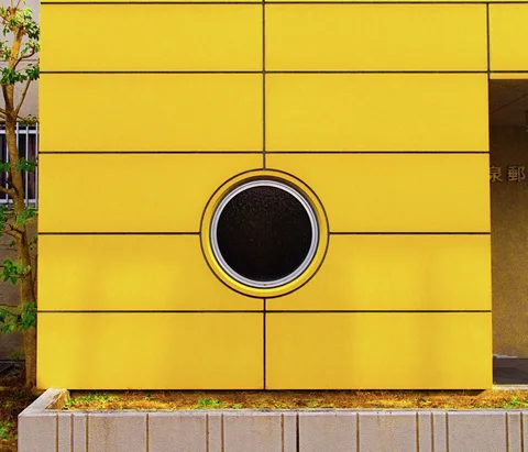 A round dark window interrupts a grid of bright yellow exterior wall panels.
