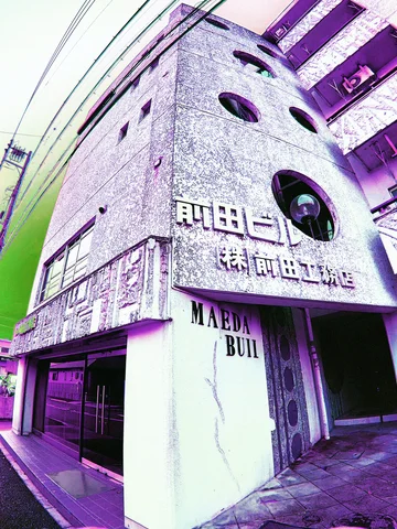 A narrow gray building has round windows and raised white lettering above its entrance.