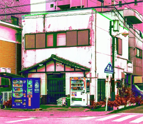 Vending machines flank a small gabled entrance beneath a weathered white corner building and overhead wires.