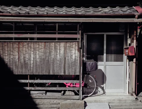 A bamboo screen and pale sliding door front a tiled-roof house beside a bicycle.