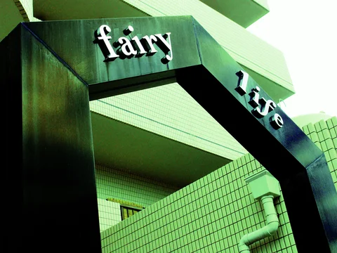 Raised white fairy and rise lettering decorates a dark angular entrance frame before pale tiled balconies.