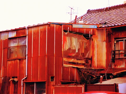 Red-toned weathered metal siding surrounds a covered window beside dark wooden house walls.