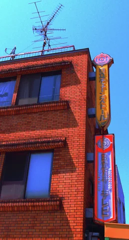 Stacked narrow vertical signs hang beside a red brick building topped with television antennas.