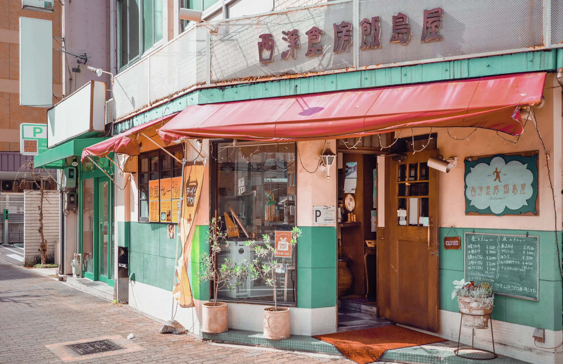 A pink awning shades a colorful corner storefront with turquoise panels, glass windows, and wooden doors.