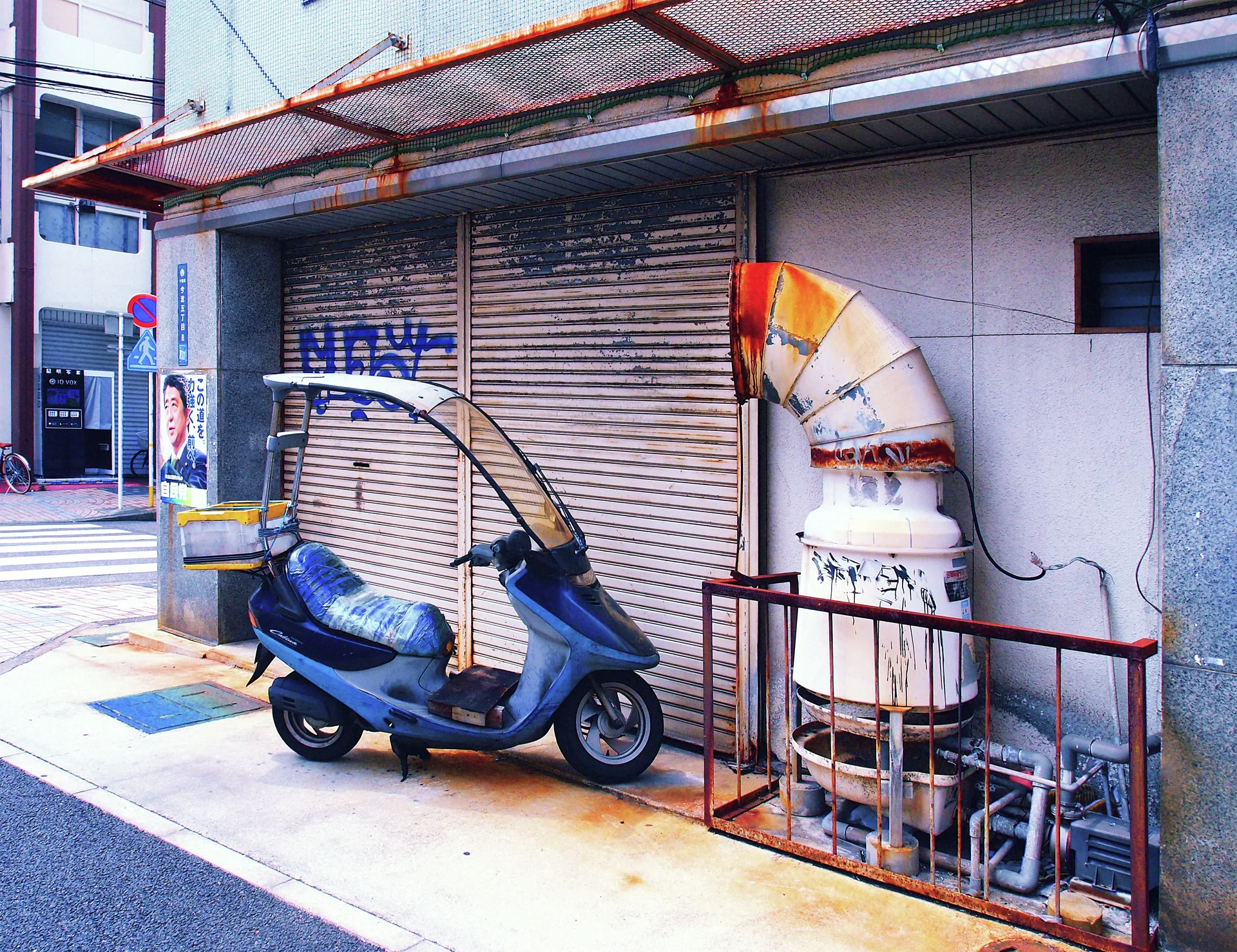 A blue scooter stands beside a shuttered storefront and a large rust-stained ventilation duct.