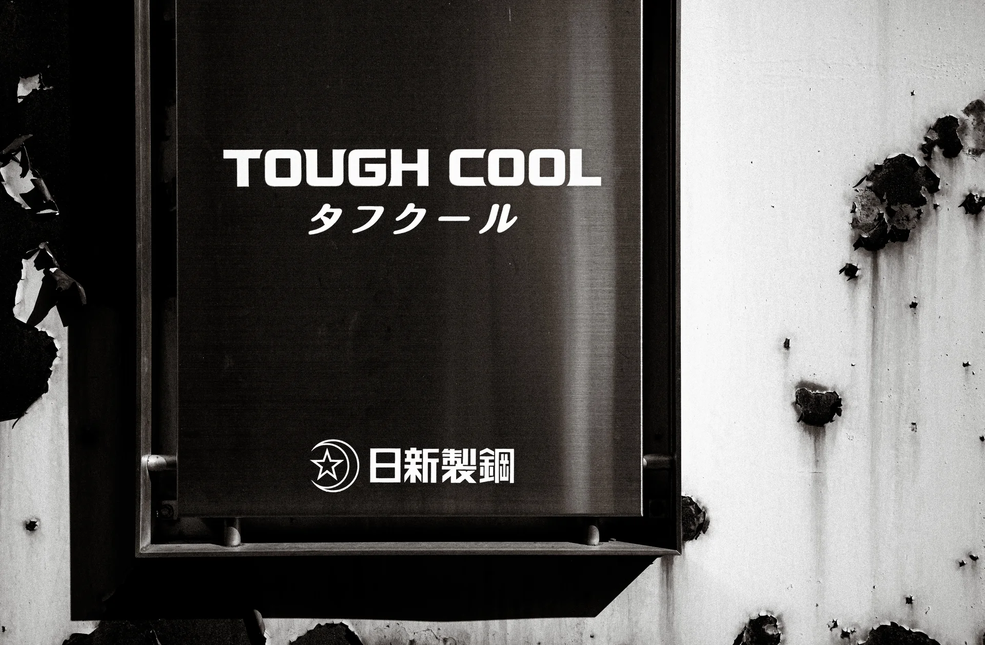 A dark TOUGH COOL sign projects from a stained pale wall in black and white.