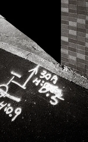 White chalk arrows and markings cover dark pavement beside a triangular patch of sunlight in black and white.