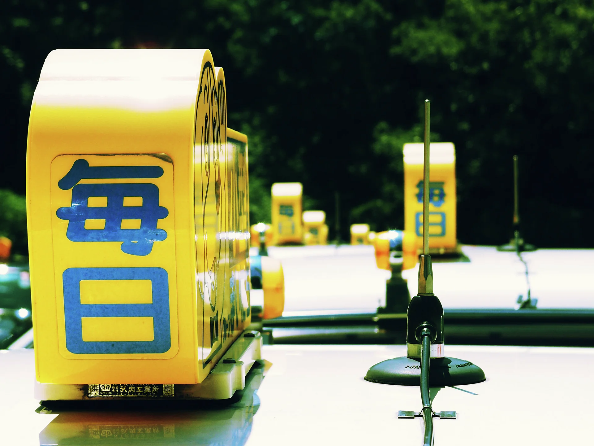 Yellow rooftop signs with blue Japanese characters repeat along a row of pale vehicles.