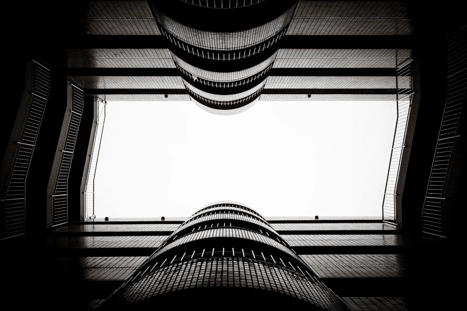 Curved balcony rails frame a bright rectangular opening overhead in a symmetrical black and white view.