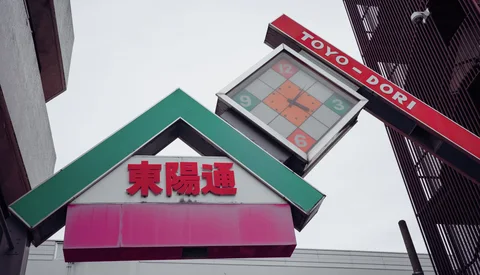 A square clock hangs above a green-roofed street sign beside a red overhead bar.