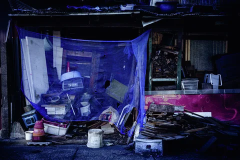 Blue mesh covers piled containers and equipment outside a cluttered weathered shed.