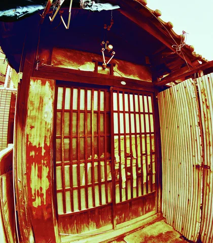 Weathered wooden lattice doors sit beneath a small tiled overhang beside rust-streaked corrugated siding.