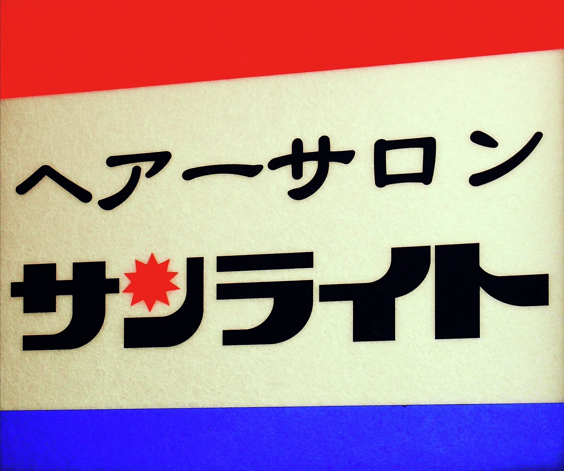 Bold black Japanese lettering and a red sunburst fill a cream sign bordered in red and blue.