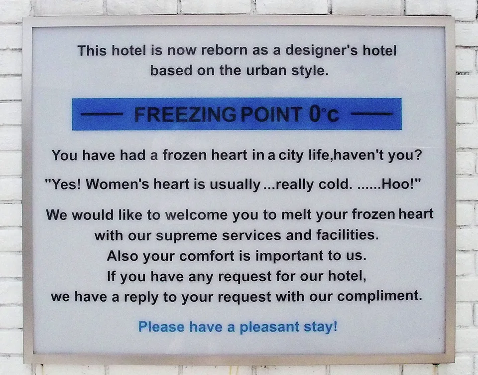 A framed English hotel notice has a blue FREEZING POINT heading against a white brick wall.