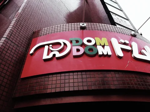 Raised colorful DOM DOM lettering curves around a red sign on a tiled building corner.