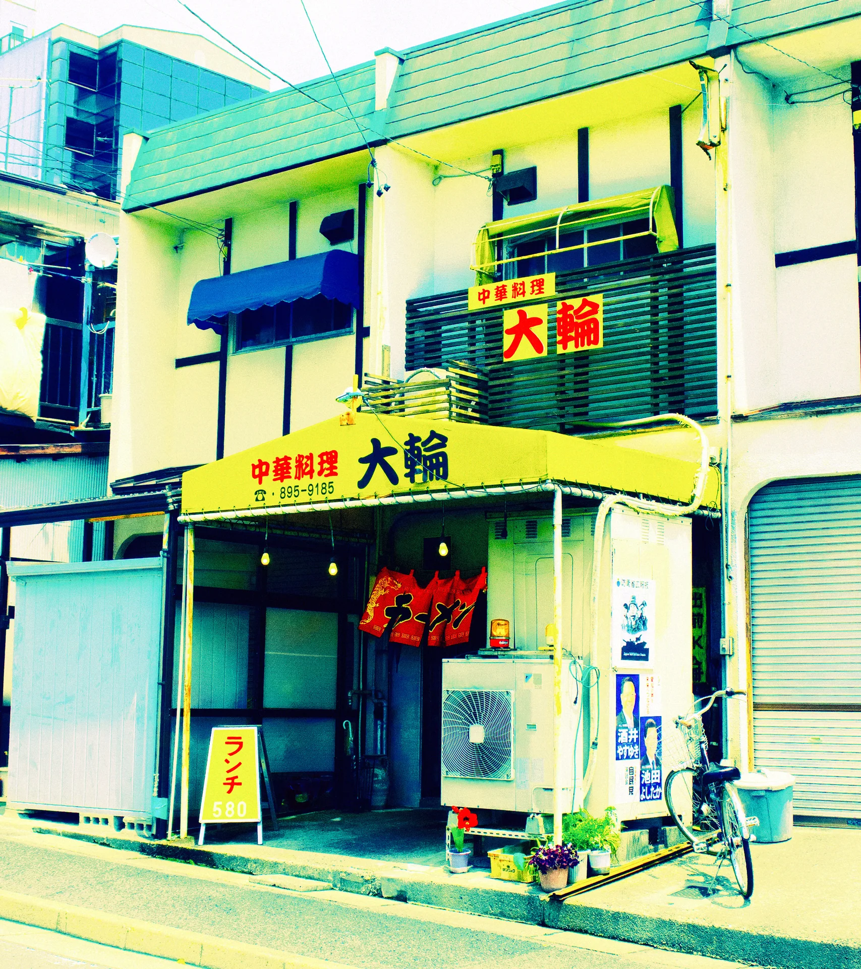 Red Japanese signage decorates a pale yellow restaurant with blue trim, hanging lanterns, and a parked bicycle.