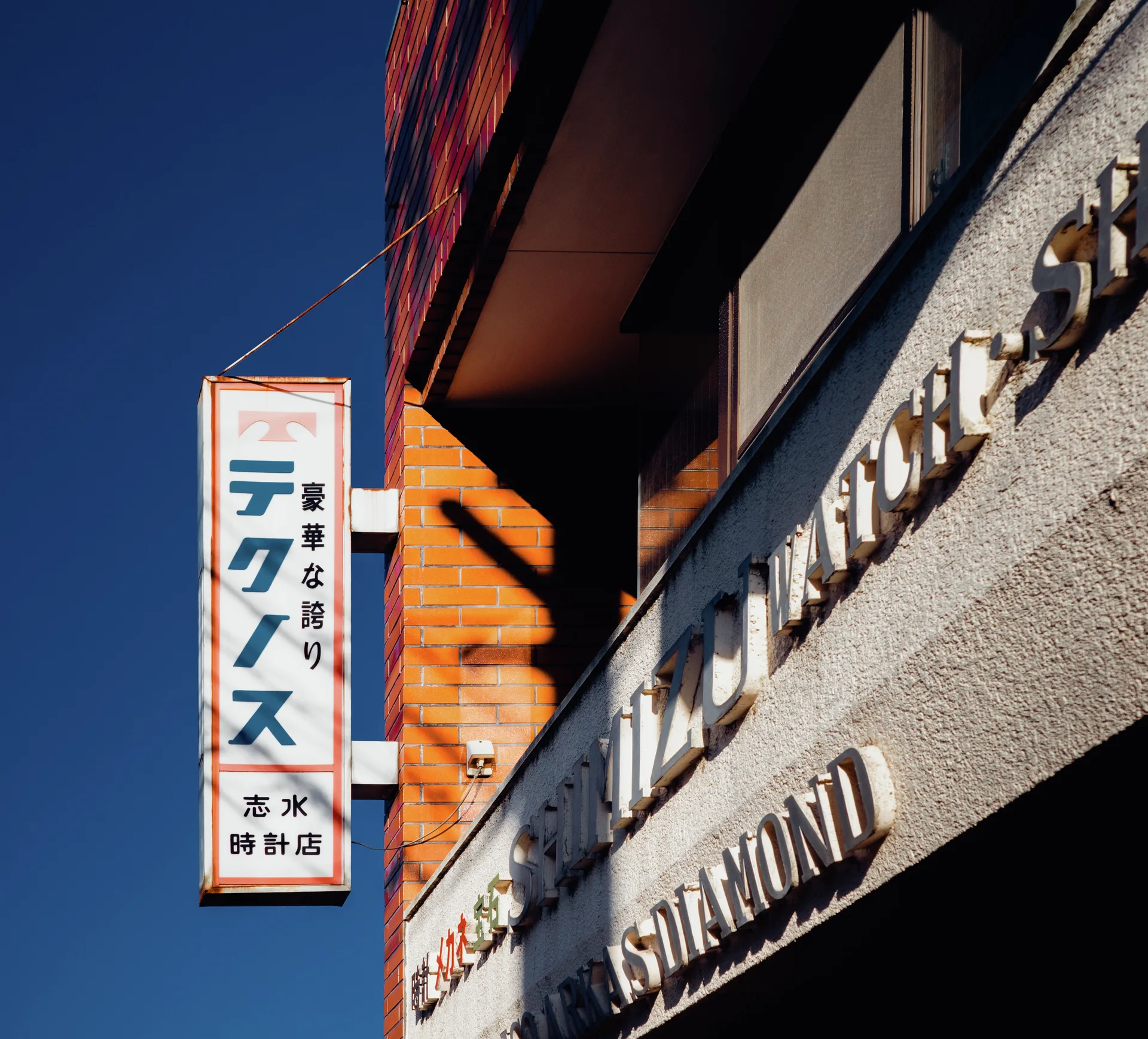 Raised metallic lettering and a projecting vertical sign catch sunlight against a blue sky.